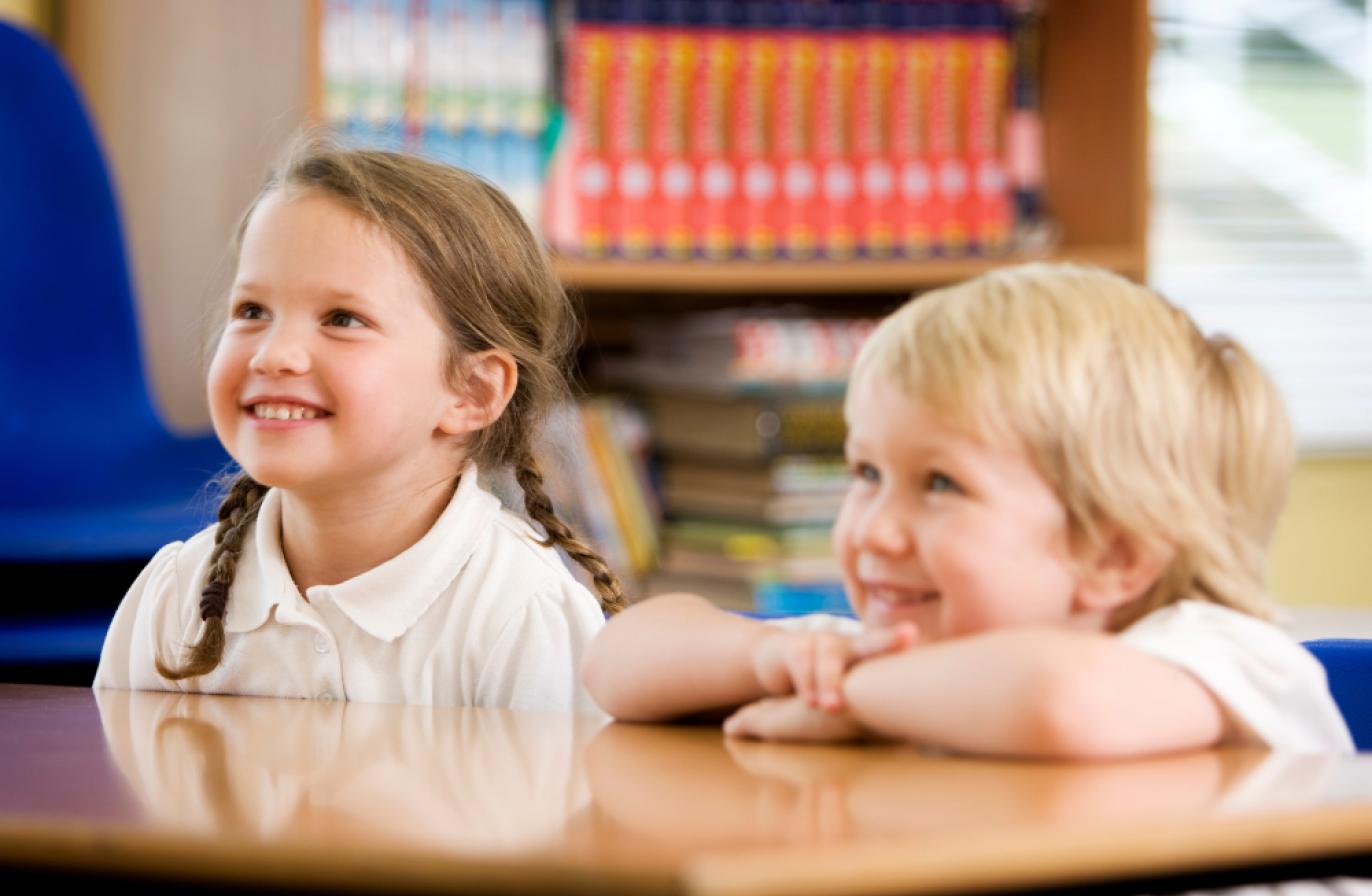 Two smiling children sat at a desk